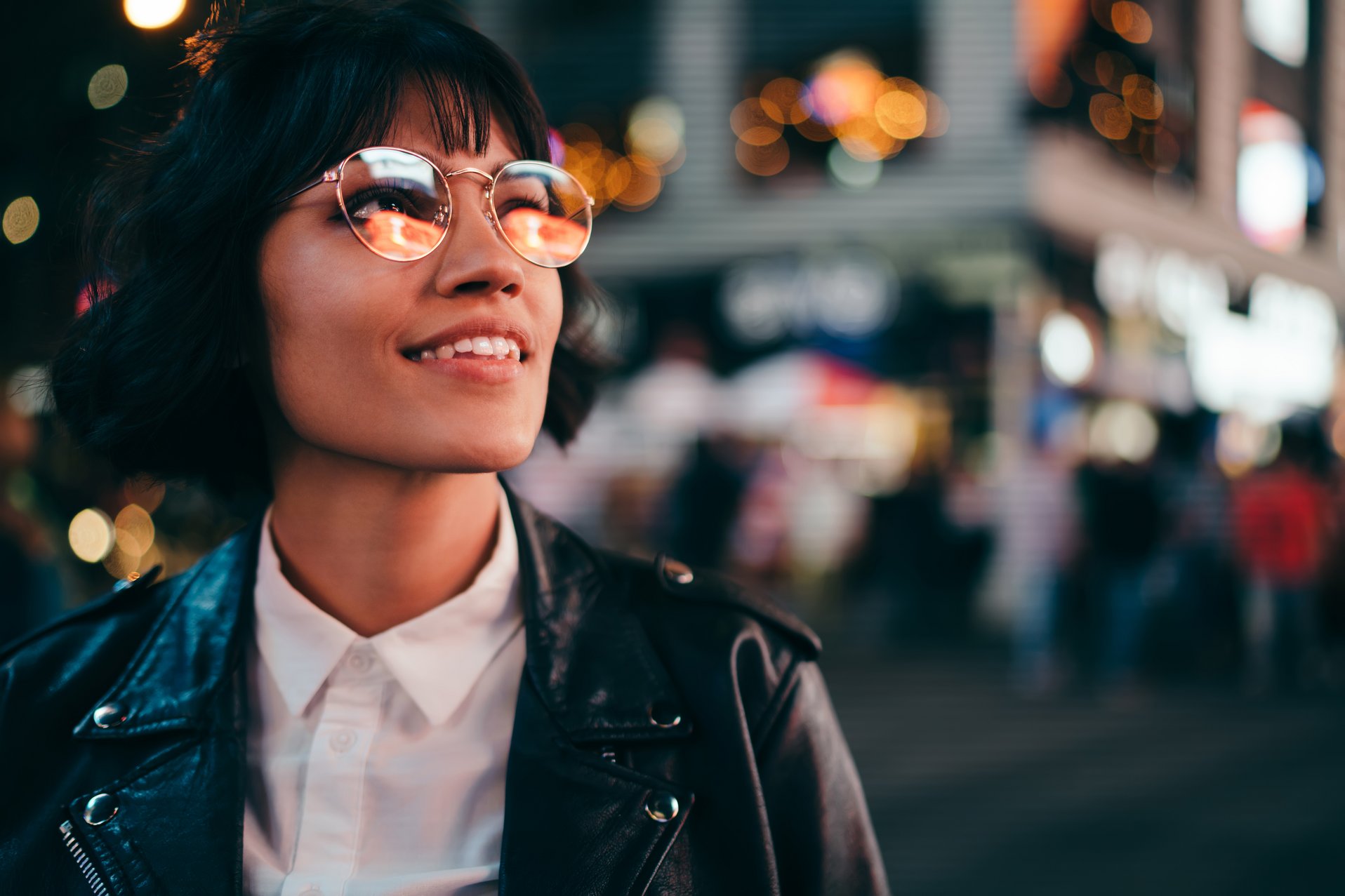 Eine Frau mit Brille, die in einer Stadt leicht nach oben schaut.